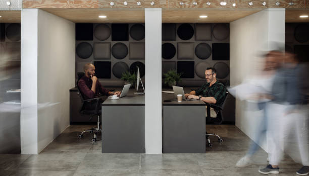 istock Two businessmen working in cubicles in a busy modern coworking office 1257729312