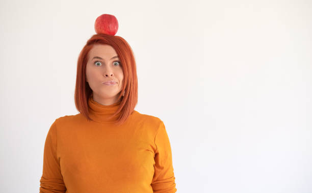 Woman making a face with red apple on top of head