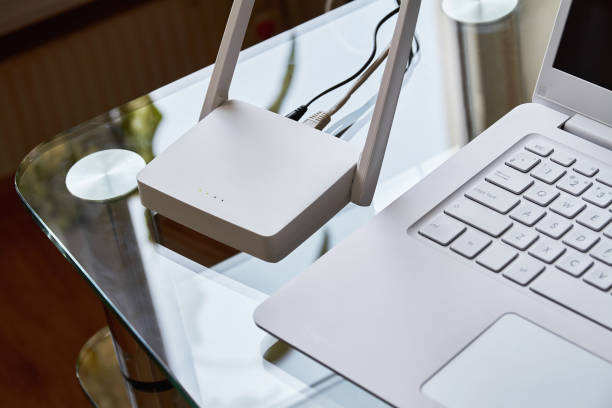 router wi-fi wireless bianco vicino a un laptop su un tavolo di vetro - interconnect order connection white foto e immagini stock
