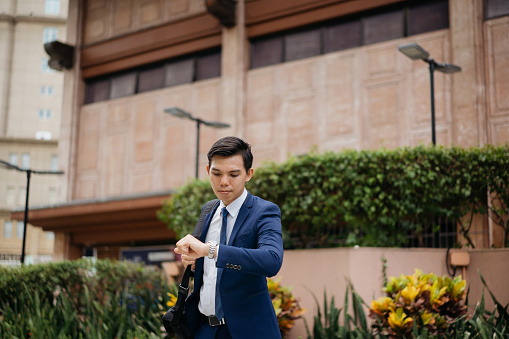 Shot of a young asian businessman looking at watch to check the time
