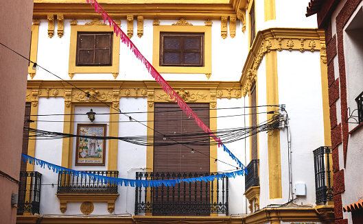 Polop de la Marina, Costa Blanca, Spain - 3 Otober 2019: Historic house facade with yellow stucco and tile painting of Siant Francesco Assisi and colorful flags