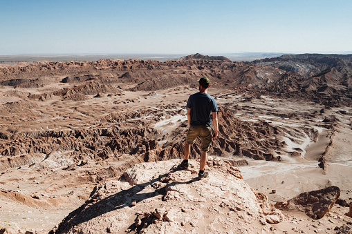 A tired man with a backpack on his back and wearing a cap climbs a desert sand hill. Rear view. Unknown person