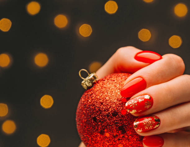 Female hand with red manicure with gold design holding Christmas ball. Female hand with professional red manicure with gold snowflakes design holding Christmas bright ball in front of blurred lights. christmas nails stock pictures, royalty-free photos & images