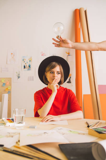 istock Young pretty girl artist in hat thinks and idea comes in studio. Insight is symbolized by a light bulb in hand 1257745525