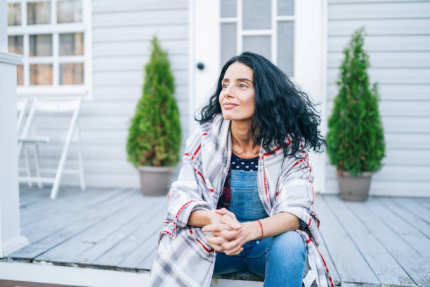 Sad mid adult woman sitting on stairs in front of her house stock photo