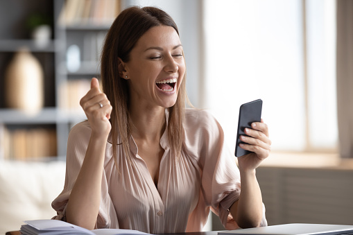 Excited happy woman looking at phone screen, celebrating online win, overjoyed young female screaming with joy, holding smartphone, reading good news in unexpected message or email