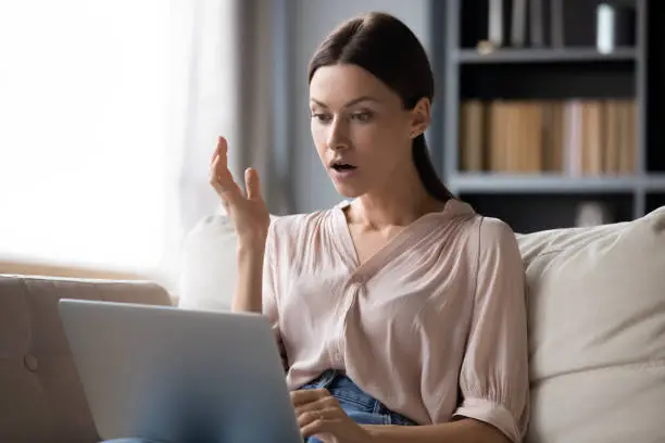 Photo of Shocked young woman looking at laptop screen, unexpected news