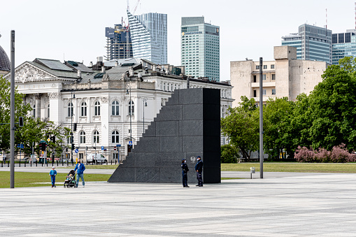 Warsaw, Poland - May 22, 2020: View of the monument commemorating the memory of the victims of the Smolensk disaster in 2010. The monument is located on Piłsudski Square in Warsaw. In the background you can see Zachęta art gallery and the line of skyscrapers. Photo was taken during the lasting SARS-CoV-2 pandemic.