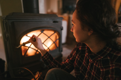 Woman sitting near wood stove  in cozy cabin