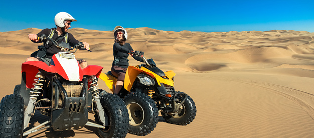 Happy couple of ATV quad bikers laughing joyful, cheerful and driving in sand dunes desert. Young active caucasian couple in outdoor activity driving quadbike in Namib desert, Namibia, Africa, near Walvis Bay, Swakopmund.