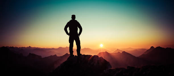 Man reaching summit enjoying freedom and looking towards mountains sunrise. Allgäu Alps, Bavaria, Germany and Tyrol Austria. stock photo