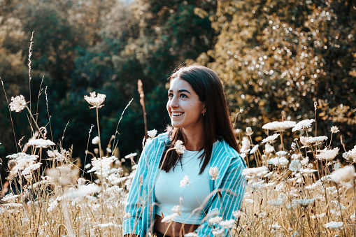 Happy smiling young teenage woman standing in summer field. Looking over to her friends with a bright happy smile.. Young Millennial Generation Female Teenage Outdoor Lifestyle Portrait.