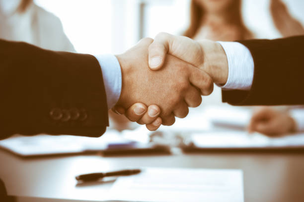 istock Business people shaking hands at meeting while theirs colleagues clapping and applauding. Group of unknown businessmen and women in modern white office. Success teamwork, partnership and handshake concept 1257761961
