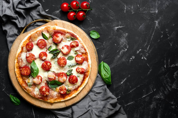 pizza italiana tradicional margherita en una tabla de cortar de madera, fondo de piedra negra. pizza con tomate, mozzarella y albahaca. vista superior, plana. - vegetarian pizza fotografías e imágenes de stock