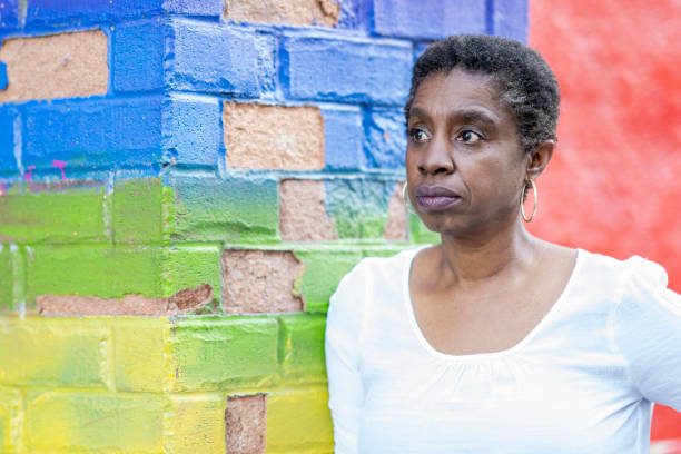 African American woman in front of a painted alleyway Portrait of a mature black woman in her 50s standing in front of a rainbow painted alleyway looking at the camera. anti racism photos stock pictures, royalty-free photos & images