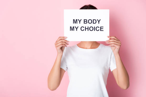 woman in white t-shirt holding placard with my body my choice lettering while covering face on pink - t shirt shirt pink blank imagens e fotografias de stock