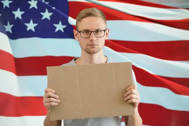 Photo of A cardboard sign in the hands of a man against the background of the american flag