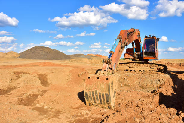 istock Excavator working on earthmoving at open pit mining on blue sky background. Backhoe digs sand in quarry. 1257773887
