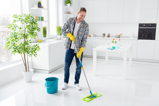 Full length body size view of his he nice attractive cheerful cheery guy husband cleansing, wiping floor preparing in big large open space modern light white interior style kitchen