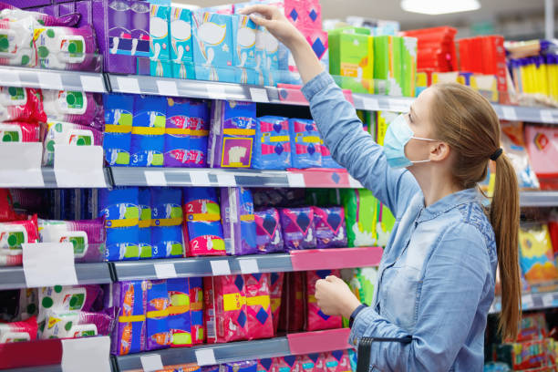 giovane donna che indossa una maschera protettiva per il viso che raggiunge la scatola dei assorbenti al supermercato - stili foto e immagini stock