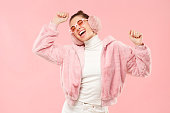 Young excited girl wearing warm furry coat, earmuffs and colored eyeglasses, moving arms to sounds of music, isolated on pink background