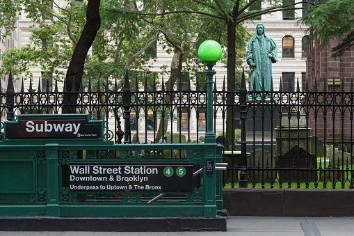 New York, New York - August 19, 2018: A view of the Wall Street Subway Station entrance in front of Trinity Church in Lower Manhattan