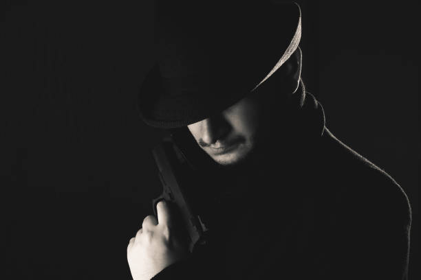 istock Retro man in coat and hat holding a gun 1257781535