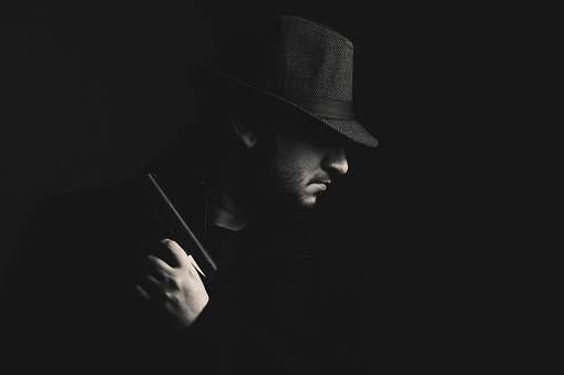 Retro man in coat and hat holding a gun, black and white. Noir style.