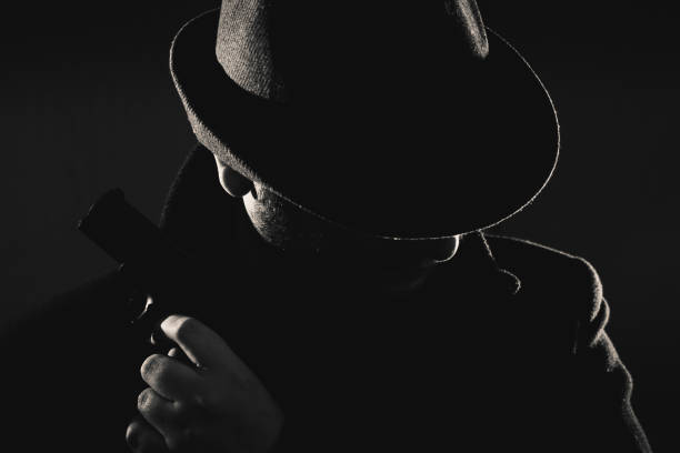 istock Retro man in coat and hat holding a gun 1257781663