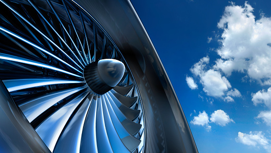 Close-up of aircraft jet engine turbine against a blue sky with white clouds