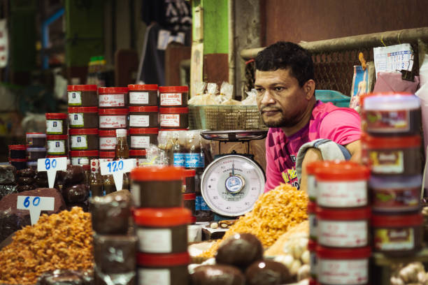 Trang city, Trang province, Thailand - June 30 2020:  Rama VI Soi 1 is the entrance to Trang Market.  A busy narrow street lined fresh food stalls and stores.  Here we see a Thai market vendor staring into space at his stall which is selling traditional shrimp paste.