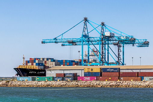 Port Adelaide, Australia - Feb 11, 2020: Flinders Ports Adelaide Container Terminal at Outer Harbour with distinctive blue gantry cranes and Kota Laris container ship at dock loading/unloading containers