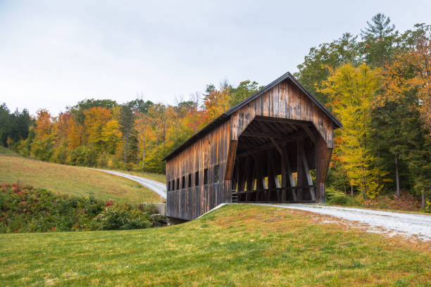 Traditional covered bridge along a gravel road with in the countryside of Vermont on a cloudy autumn day. Beautiful fall colors. Woodstock, VT, USA.