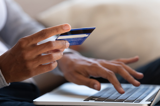 Close up of black girl hold bank credit card and type on laptop, shopping online using computer, buying goods or ordering online, entering bank accounts and details in online banking offer