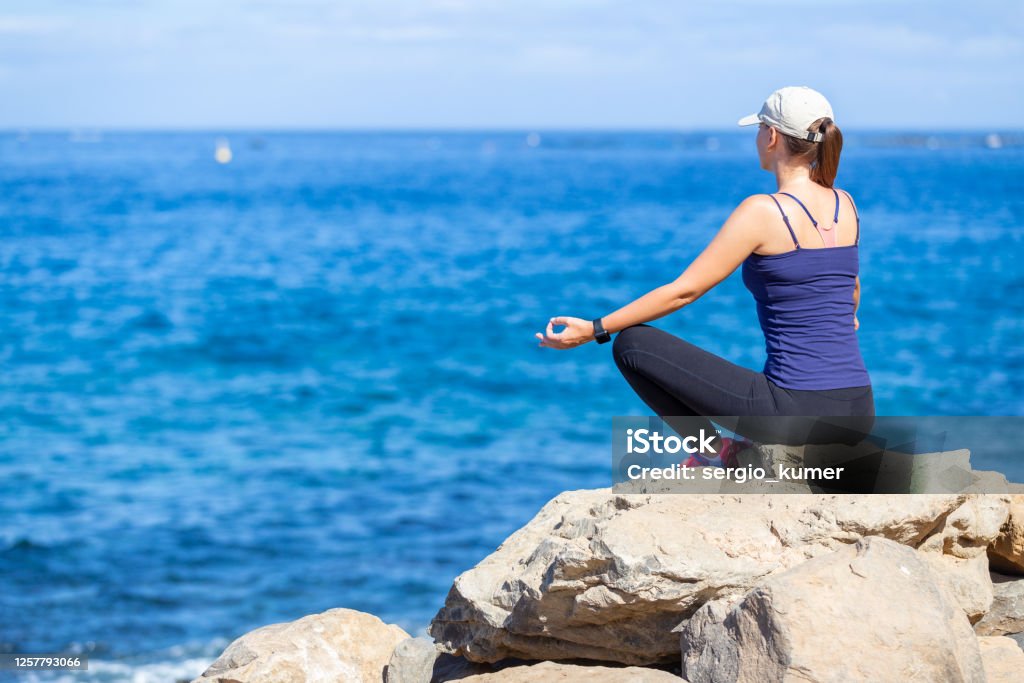 Young woman relaxing in yoga pose near the ocean Young sporty woman relaxing in yoga pose and looking on the ocean. Back view of meditation girl 30-39 Years Stock Photo