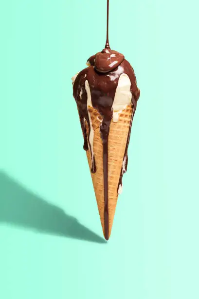 Vanilla ice cream cone with melted chocolate topping, isolated on green mint background, in harsh light. Summer dessert. Dripping chocolate sauce