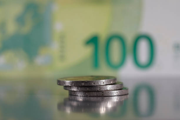 One small pile of three coins have been stacked on a grey, flat surface and it is visible against a blurred 100 euro banknote.
