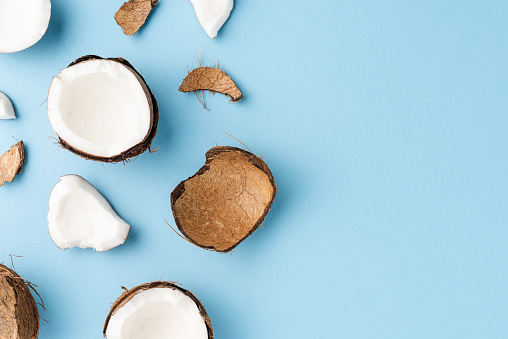 Fresh cracked coconut on blue background with copyspace. Flat lay