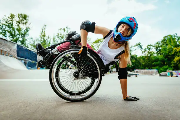 Generation Z woman in wheelchair practicing stunts in skate park. Determination, courage and confidence shown in this extreme sport done by disabled woman.