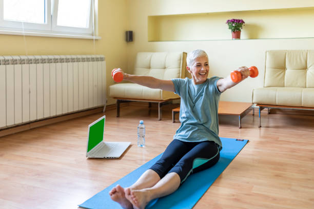 istock Sporty elderly lady training at home with dumbbells, watching online tutorials on laptop, copy space 1257809745