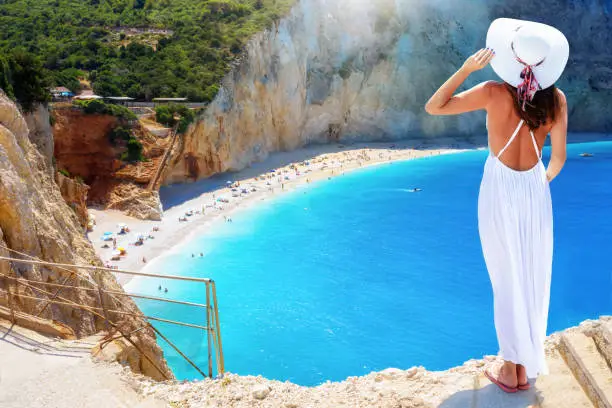 A beautiful tourist woman with white hat looks at he famous beach of Porto Katsiki, Lefkada, Greece, during her summer vacation time