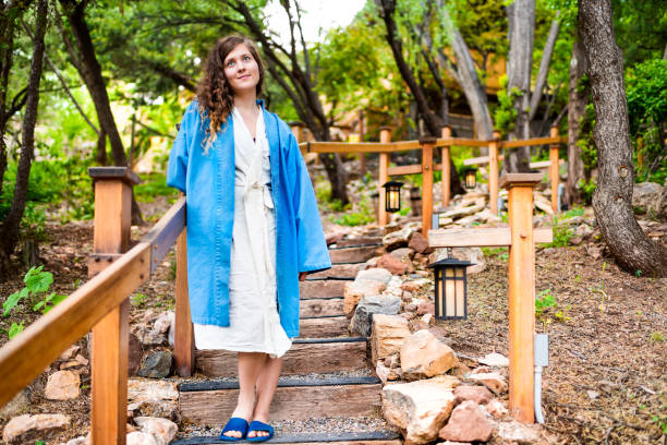 Japan onsen in evening with illuminated hanging lantern lamp light on wooden pole post in Japanese garden with steps stairs and woman in kimono robe standing looking up