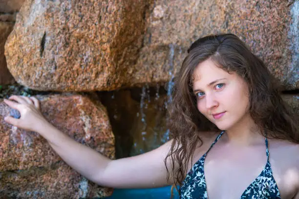 Young woman face portrait closeup happy smiling by waterfall on rocks in wellness spa with blue water and wet long hair