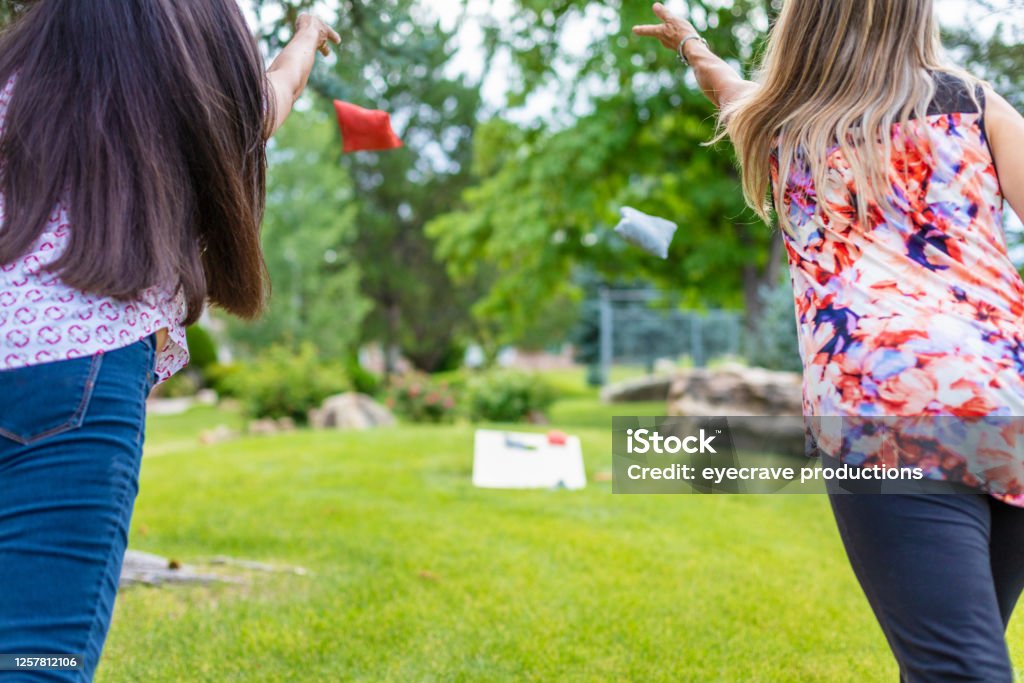 Two Adult Senior Female Friends Having Fun Together Outdoors In Western Colorado Two Adult Senior Female Friends in focus in foreground with backs to camera Having Fun Together Outdoors Playing Bean Bag Toss Corn Hole Game in lush green setting with bean bag and game board blurred in background Part of Two Adult Senior Female Friends Having Fun Together Outdoors Series 4K Video Also Available for this Photo Series (Shot with Canon 5DS 50.6mp photos professionally retouched - Lightroom / Photoshop - original size 5792 x 8688 downsampled as needed for clarity and select focus used for dramatic effect) Bean Bag Toss Stock Photo