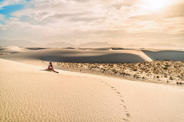 giovane ragazza donna sulla sabbia in sabbia bianca dune monumento nazionale in new mexico seduto su slitta disco per scivolare giù per la collina durante il tramonto tono vintage - sliding sands foto e immagini stock