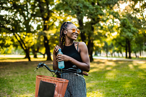 Photo of a young African American woman leaning on her bicycle with water