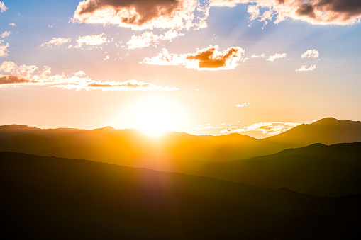 Yellow orange colorful sunset with sun rays flare in Aspen, Colorado USA with aerial view on Rocky Mountains Peak mountain ridge silhouette clouds at twilight