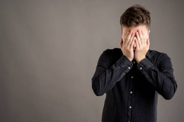 Portrait of serious stylish attractive man dressed with a casual black shirt covering eyes like blind gesture Portrait of serious stylish attractive man dressed with a casual black shirt covering eyes like blind gesture isolated on grey background with copy space advertising area hair covering eyes stock pictures, royalty-free photos & images