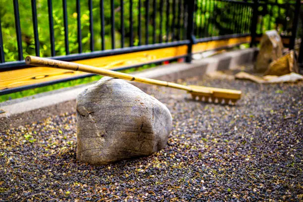 Outdoor zen rock garden in Japan temple with rake closeup on stone and pattern on gravel with fence and green foliage background and nobody