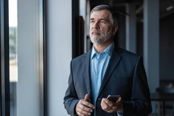 istock Businessman using mobile phone app texting. Mature caucasian man holding smartphone for business work 1257814455